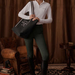 Woman holding a tote bag in a room with brown curtains and vintage furniture.