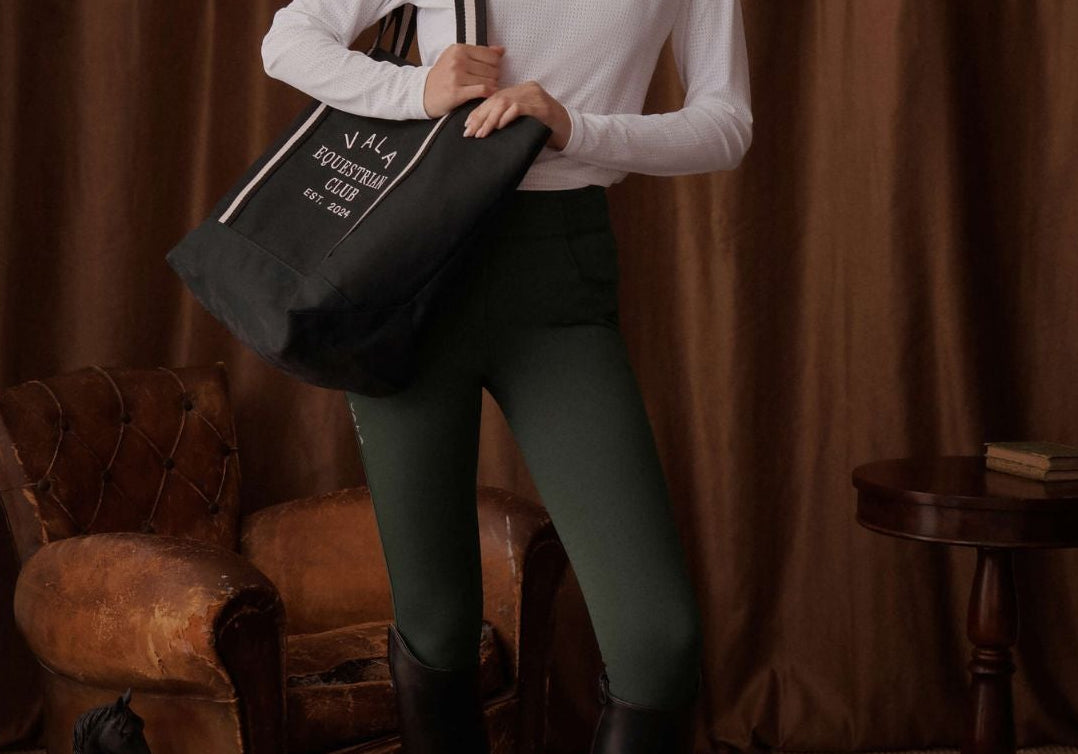 Woman holding a tote bag in a room with brown curtains and vintage furniture.