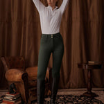 Woman in a white shirt and green pants standing in a room with brown curtains and vintage furniture.