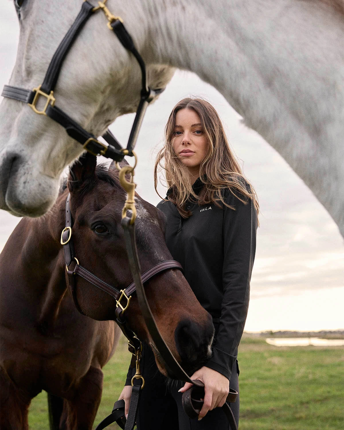 Woman in a black long sleeve riding top with two horses 