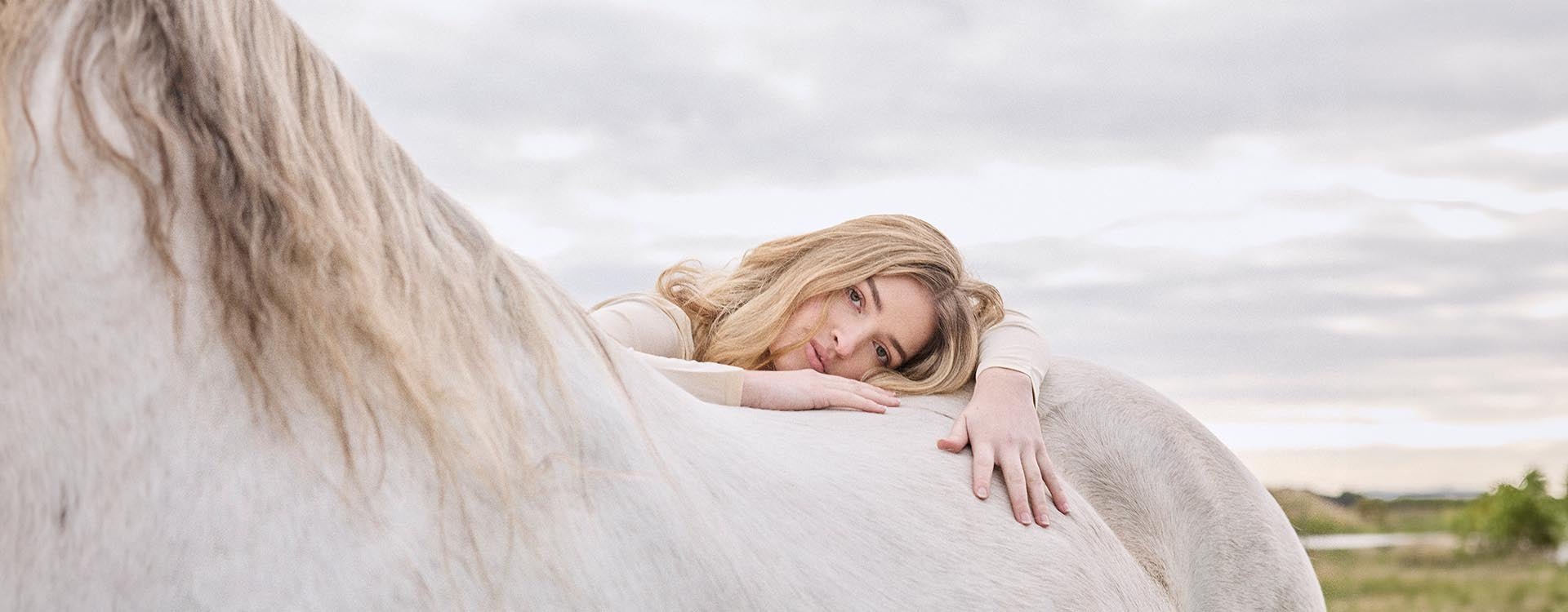 Woman wearing a cream long sleeve top with a horse 