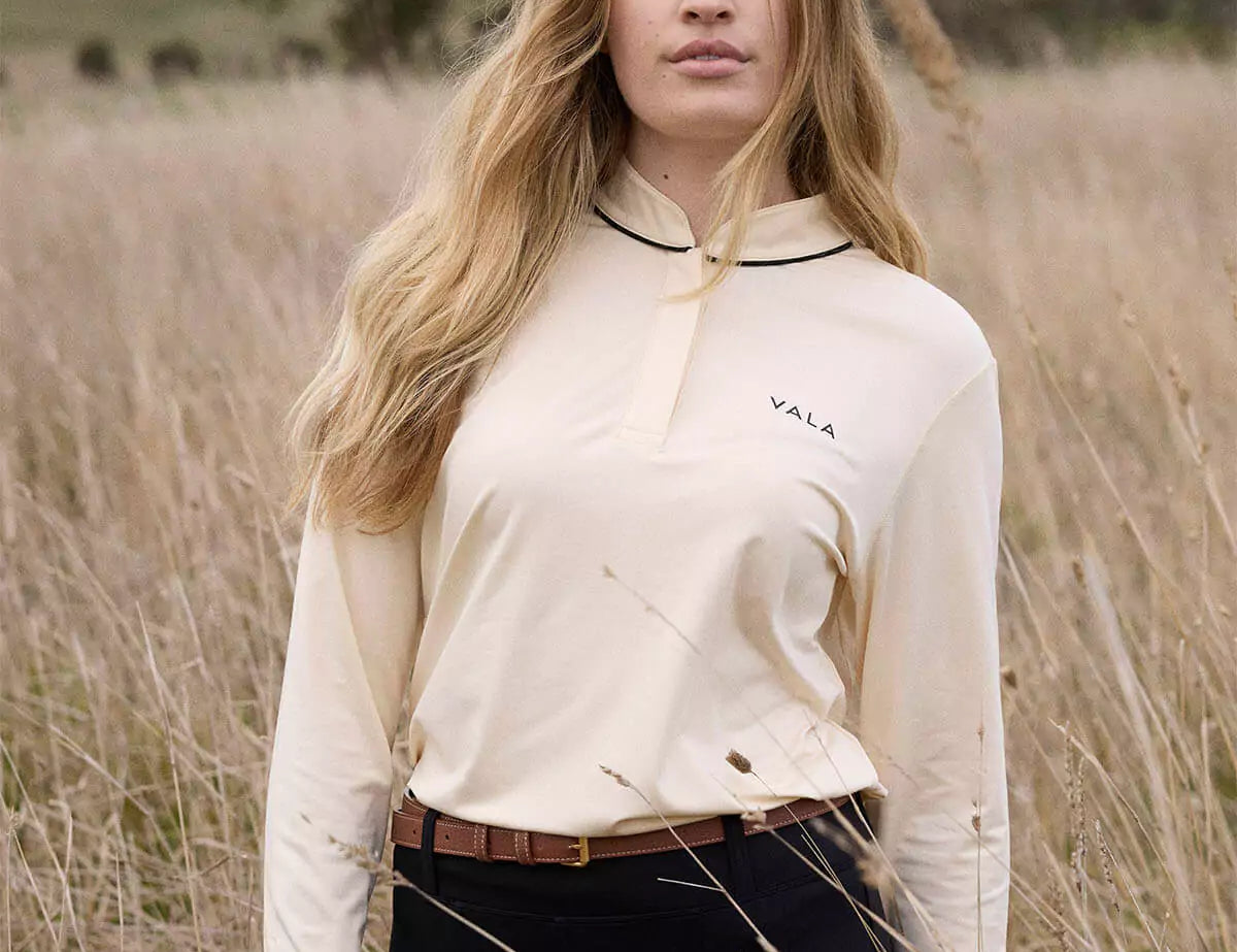 Woman in a field in a white long sleeve horse riding polo top 