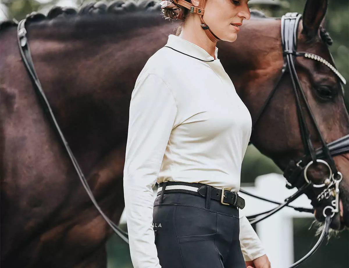 Female in a white riding top with black jodhpurs with a horse 